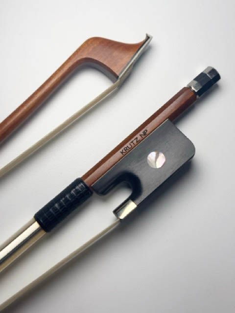 Two violin bows lying on a white surface; one has a wooden frog and the other has a black frog engraved with KRUTZ NP. Both have white horsehair and visible winding.