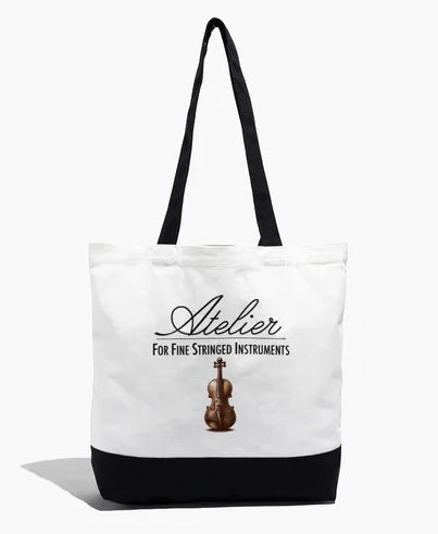 The Atelier Logo Cotton Tote Bag features a white and black cotton design with an image of a violin and the text “Atelier For Fine Stringed Instruments” on the front. Ideal for use as a violin tote or for carrying string instrument accessories, this bag is designed with long black handles and a durable black bottom.