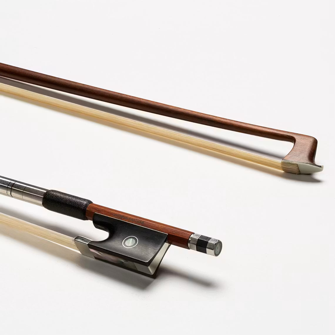 Two wooden string instrument bows with light-colored horsehair rest on a white surface. The bottom is likely an Andreas Eastman BL80 Pernambuco Violin Bow - 4/4, featuring a metal grip, decorative circle, and silver end.