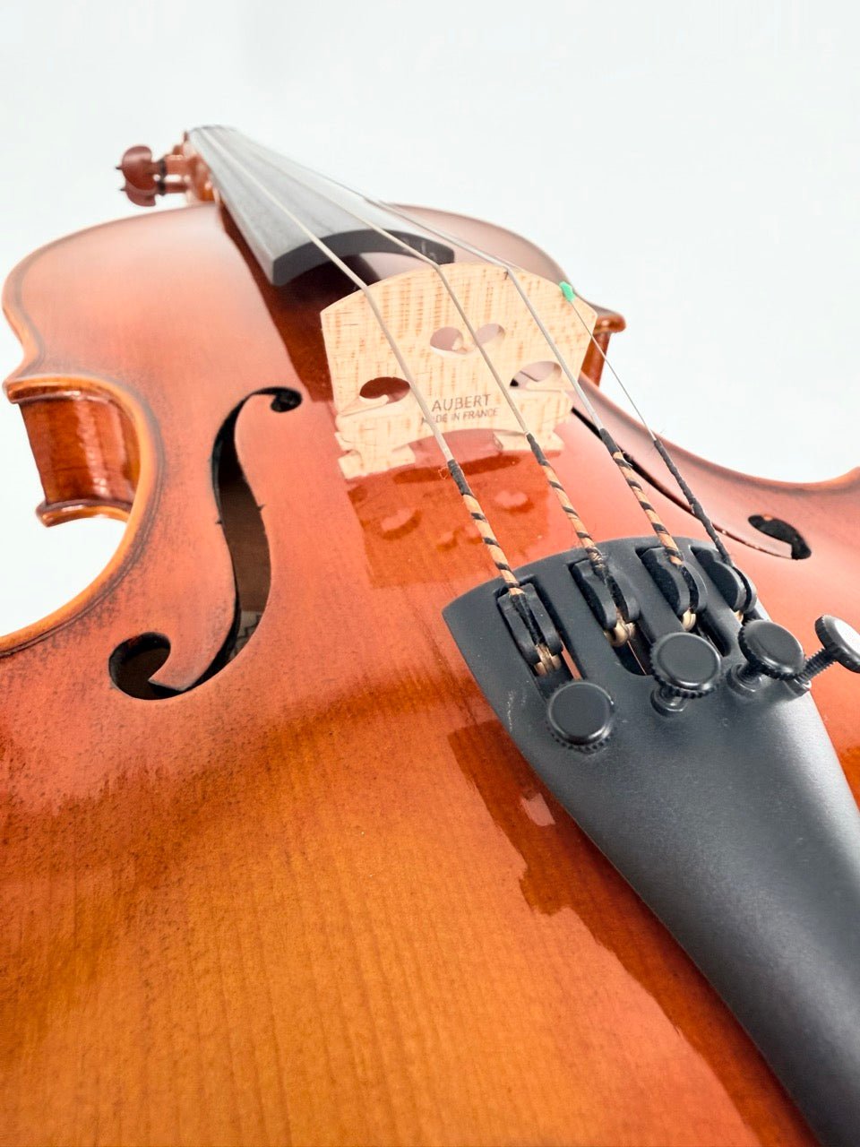 Close-up of the Atelier Violin Outfit Special, handcrafted from European tonewoods. The image highlights the bridge, strings, and tailpiece, with a warm brown finish and visible wood grain against a softly blurred background.