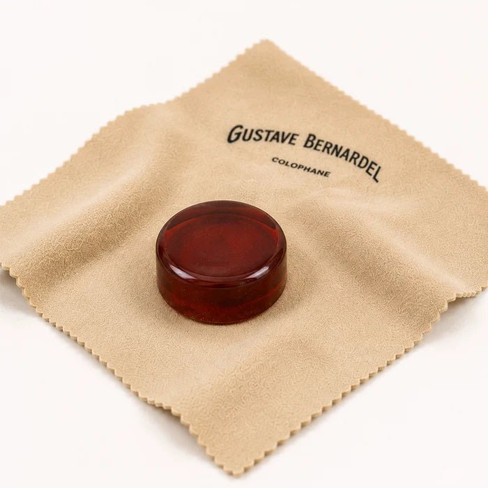 A round cake of Bernardel Rosin for Violin Viola or Cello centered on a tan cleaning cloth with the brand name printed on the corner.