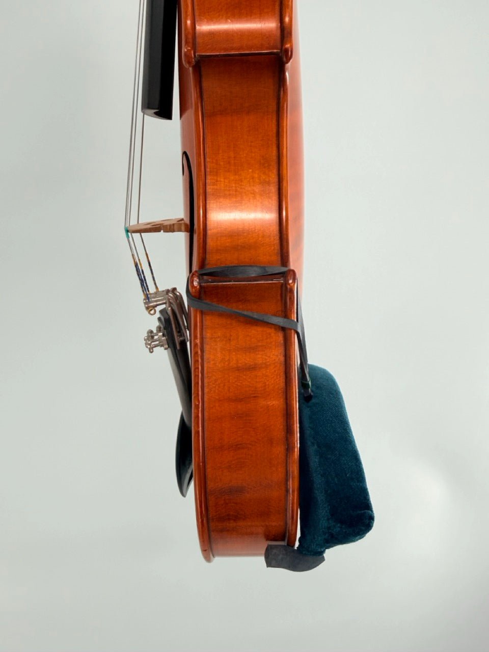 Side view of a violin with the Decor / FOM Shoulder Rest for Violin in dark blue attached, photographed against a plain light background. The strings, fine tuners, and chin rest are visible.