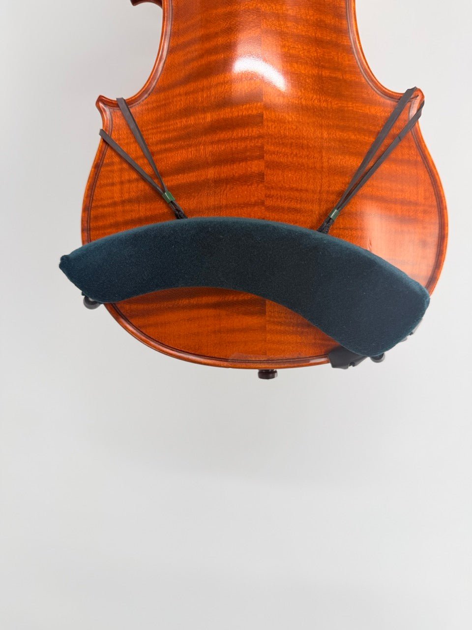 Close-up of a violin's back fitted with the Decor / FOM Shoulder Rest for Violin, secured by two elastic bands, against a plain light background.