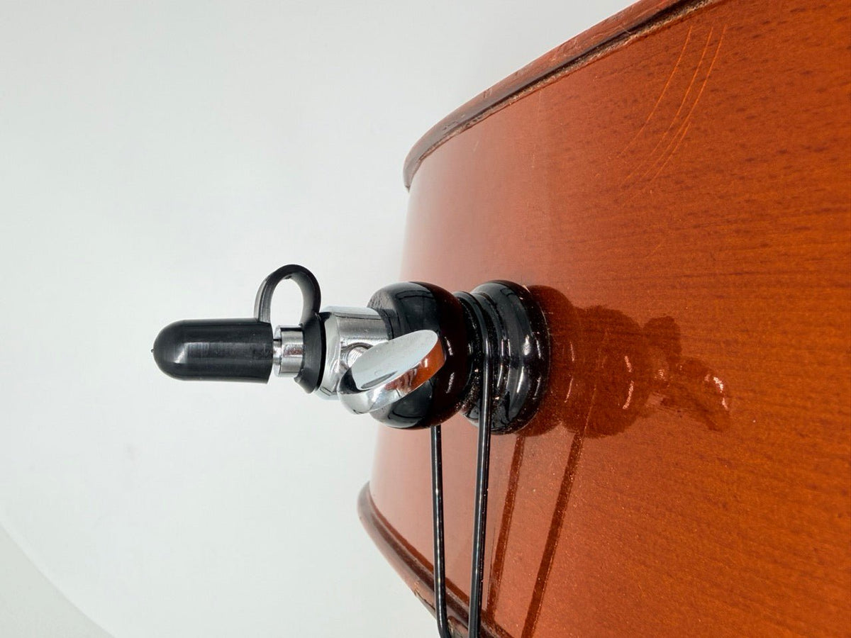 Close-up of a cello’s polished brown wooden body showing visible grain, with a black Gewa Rubber End Tip (Removable) extending from the bottom against a white background.