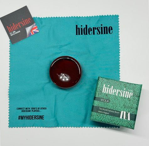 A container of Hidersine 1VA Viola Rosin – Light Amber, Large Cake rests on a turquoise cleaning cloth, accompanied by its green box packaging and a small Hidersine information card—an essential addition to any collection of quality viola accessories.