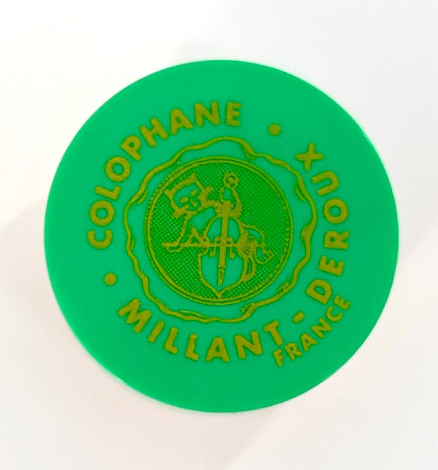 A green circular container of Millant-Deroux “Tutti” Double Bass Rosin, featuring yellow COLOPHANE MILLIANT-DEROUX FRANCE text and a central lyre-logo with ribbon, photographed from above on a white background.