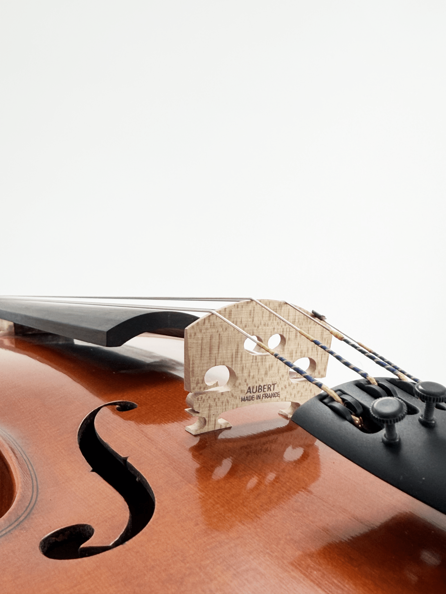 Close-up of the Octav Mures Viola’s bridge marked "Aubert Made in France," with strings, fingerboard, f-hole, and fine tuners on the tailpiece against a white background—showcasing this quality fine stringed instrument.