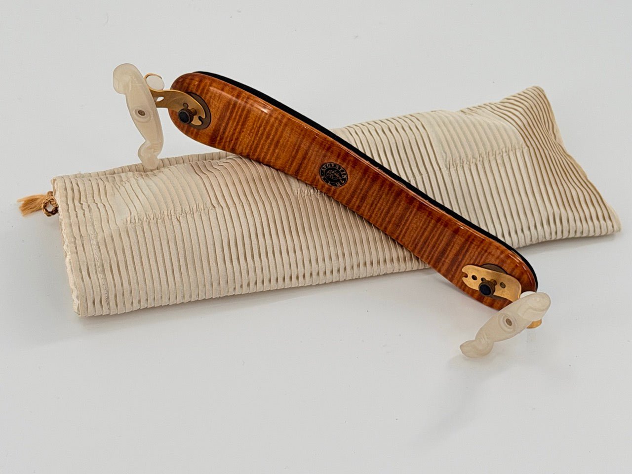 A Viva La Musica Diamond Shoulder Rest, European-made with beige plastic fittings, is displayed on a cream ribbed fabric pouch against a plain white background.