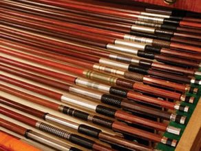 A drawer filled with neatly arranged pool cues, each with different colored and designed handles, showcasing a variety of wood tones and metal finishes.