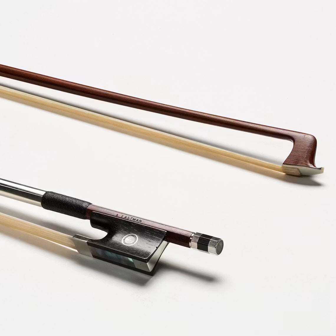 An Eastman BL60 IPE Violin Bow lies diagonally on a white surface. The close-up showcases the frog, grip, and screw—highlighting its quality features for advancing students.
