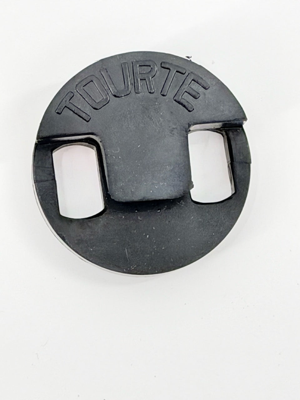 A Tourte Bass Mute, round and black with "TOURTE" embossed on top, rests on a white surface.
