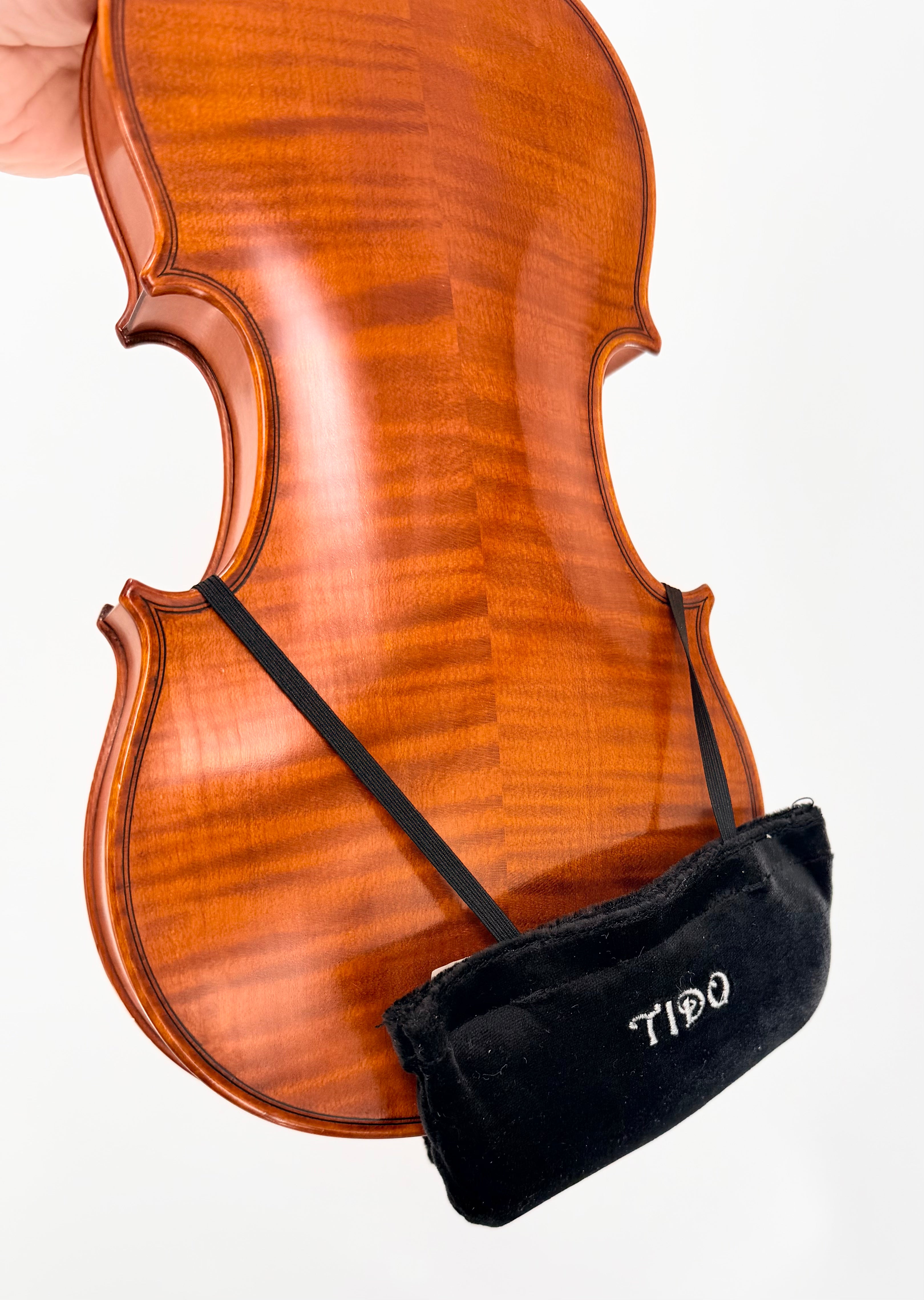 A close-up shows the Tido Universal Chinrest & Shoulder Pad for Violin and Viola in a black velvet pouch, attached by two elastic bands across the lower bout of a violin, set against a white background.