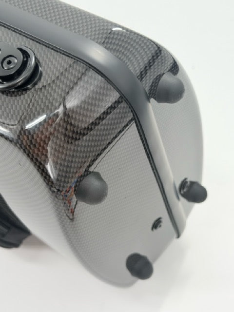 Close-up of a gray carbon fiber Otto Musica Mirage CN-512 Oblong Violin Case, featuring four black rubber bumpers and a black circular component, set against a white background.
