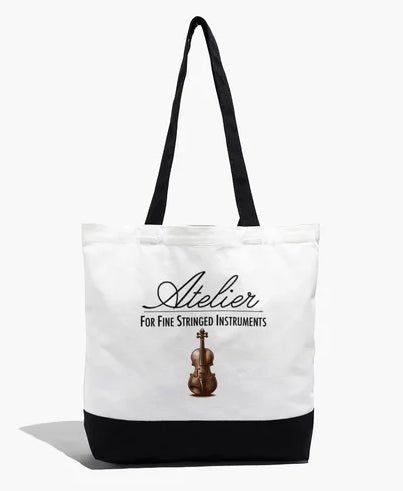 The Atelier Logo Cotton Tote Bag features a white and black cotton design with an image of a violin and the text “Atelier For Fine Stringed Instruments” on the front. Ideal for use as a violin tote or for carrying string instrument accessories, this bag is designed with long black handles and a durable black bottom.