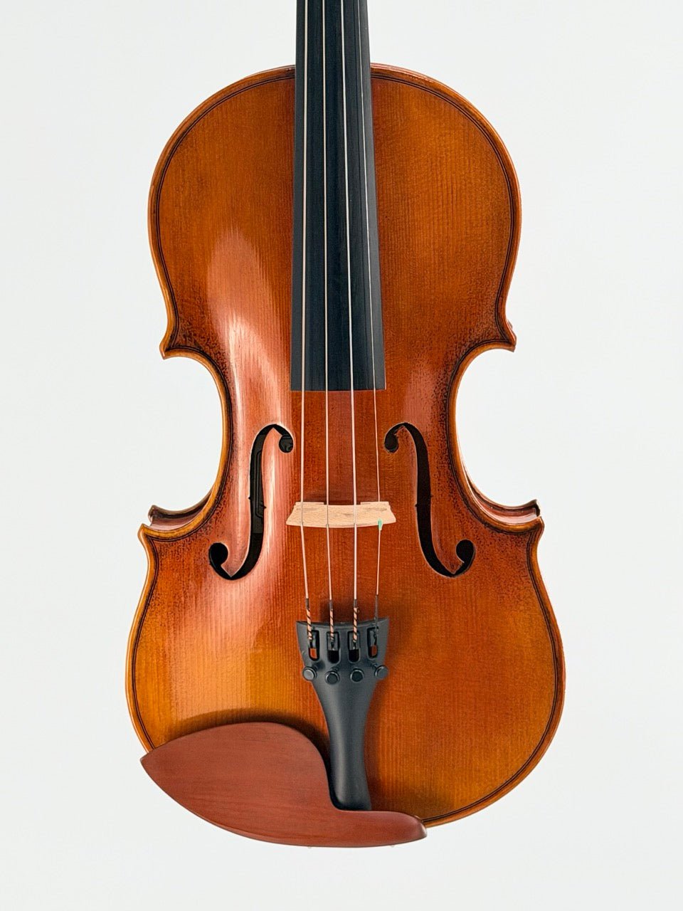 A close-up of a handcrafted violin with a rich brown finish, showing strings, bridge, and chinrest against a plain background—ideal for anyone interested in the Atelier Violin Outfit Special or seeking a quality beginner violin.