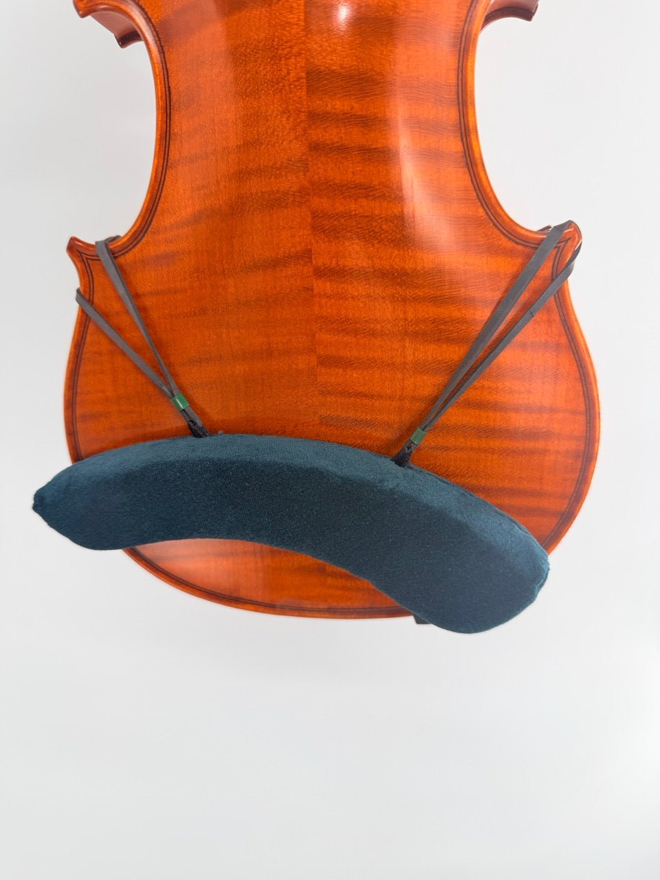Close-up of a glossy, reddish-brown violin back with a Decor / FOM Shoulder Rest for Violin, attached by two elastic bands for added comfort.