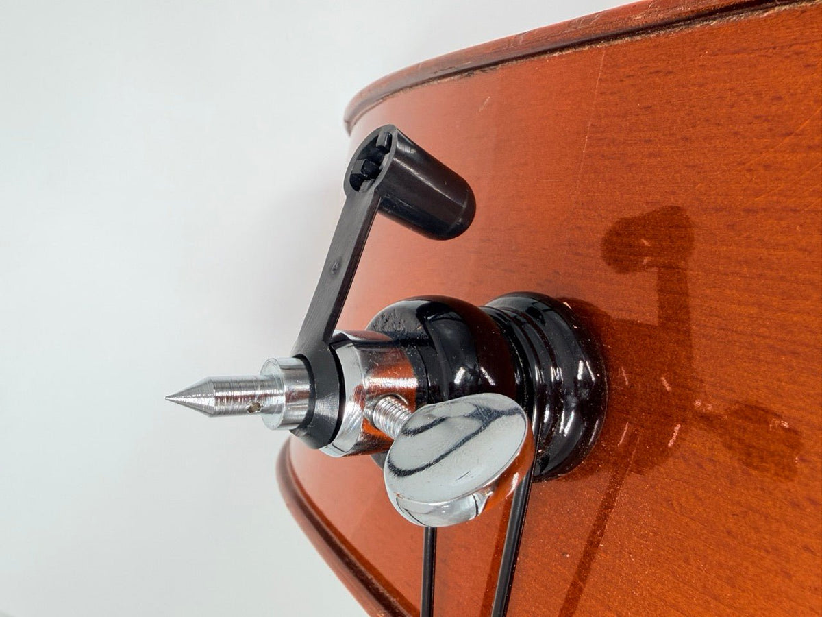 A close-up of a string instrument’s tuning peg with a crank handle attached, showcasing wood grain and metal parts, next to a Gewa Rubber End Tip (Removable) on a plain background.