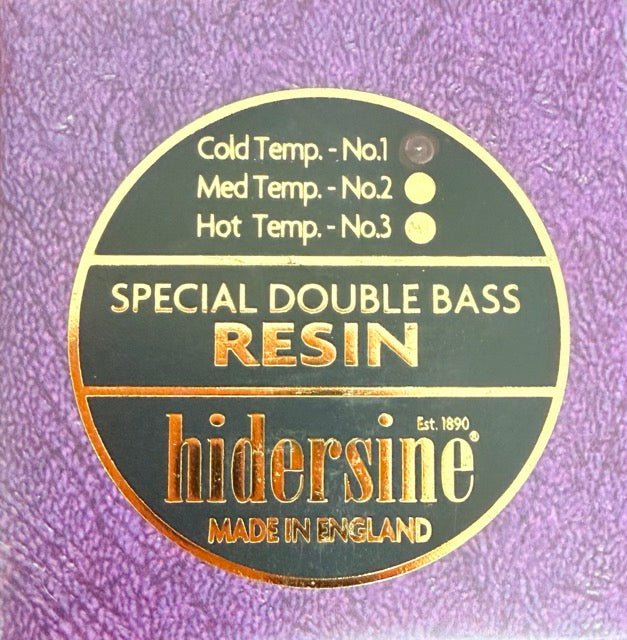 A round label on a purple background reads: Hidersine Bass Rosin, Special Double Bass Resin, Made in England, with indicators for cold, medium, and hot temperatures—ideal for double bass players seeking quality rosin.