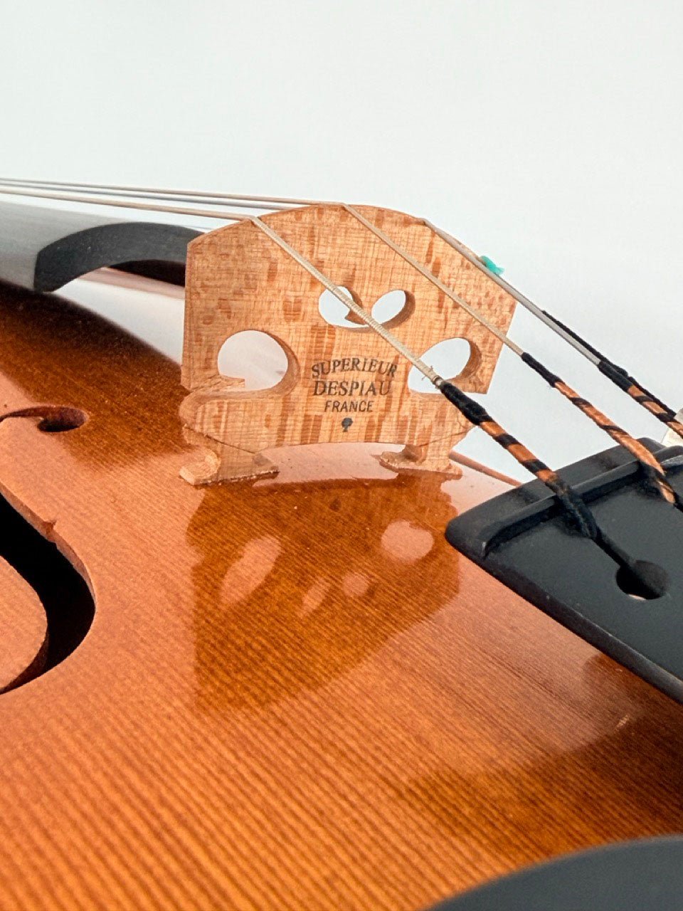Close-up of a violin bridge with the text Superieur Despiau France engraved, showing violin strings and part of the wooden body of the Luce Sebastian Professional Instrument, handcrafted from premium tonewoods and ideal for those seeking a professional-level violin.