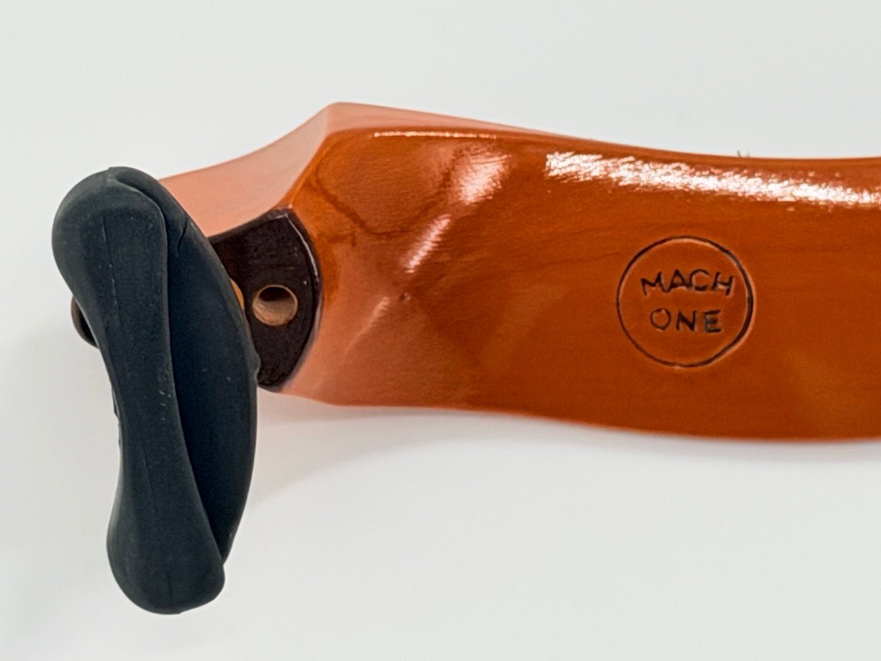 Close-up of a shiny brown Mach One MA Maple Shoulder Rest – Premium Wooden Violin Support (4/4–3/4) with a black curved handle and MACH ONE stamped on the surface. The support is made from premium maple wood.