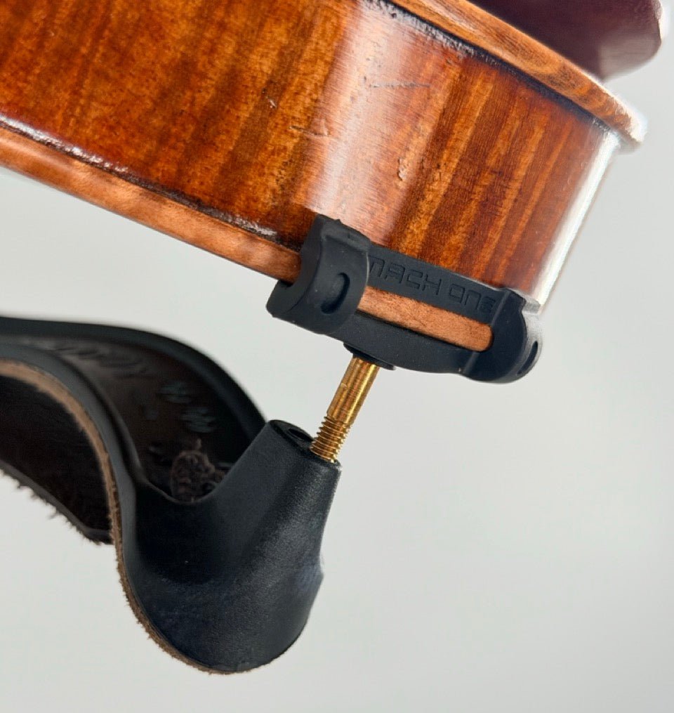 Close-up of a violin’s chin rest with screw and black brackets, showing wood grain and curved edges, next to the Mach One MLS Shoulder Rest with Leather Strap (Plastic) – a lightweight violin support for 4/4–3/4 instruments.