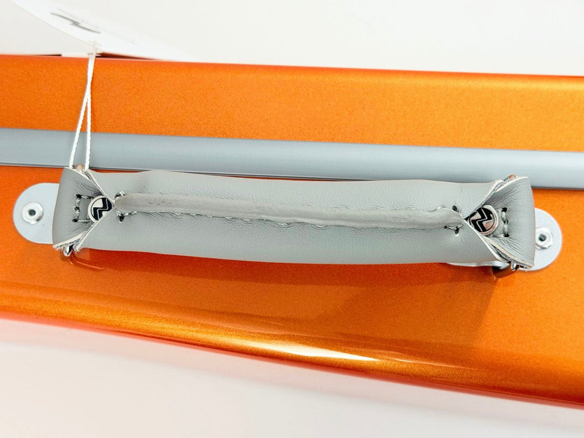 A close-up of a gray padded handle attached with string to the orange metallic surface of the Negri Eternity Carbon Fiber Shaped Violin Case in Fury Orange.
