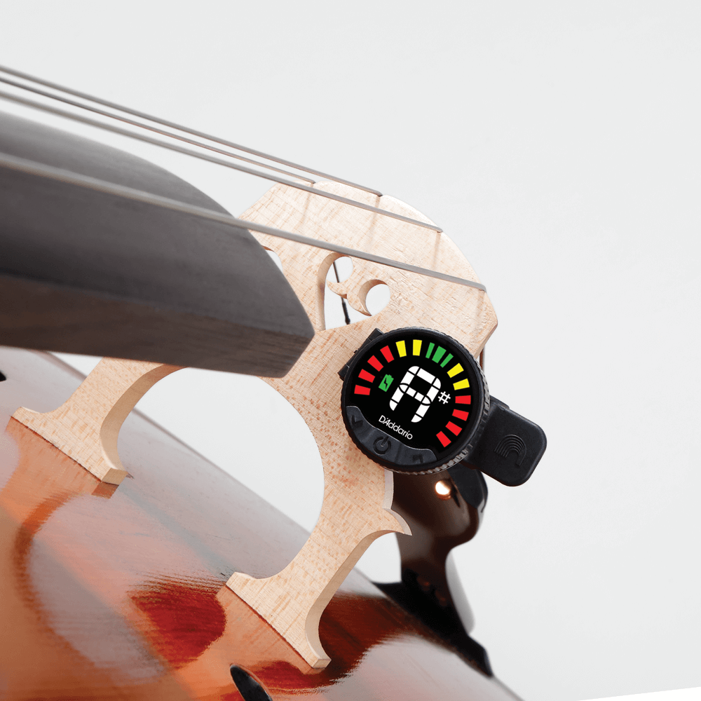 A close-up of a cello bridge with the Nexxus 360 Cello & Bass Rechargeable Tuner attached, showing tuning information with colored lights and a note symbol on its screen.