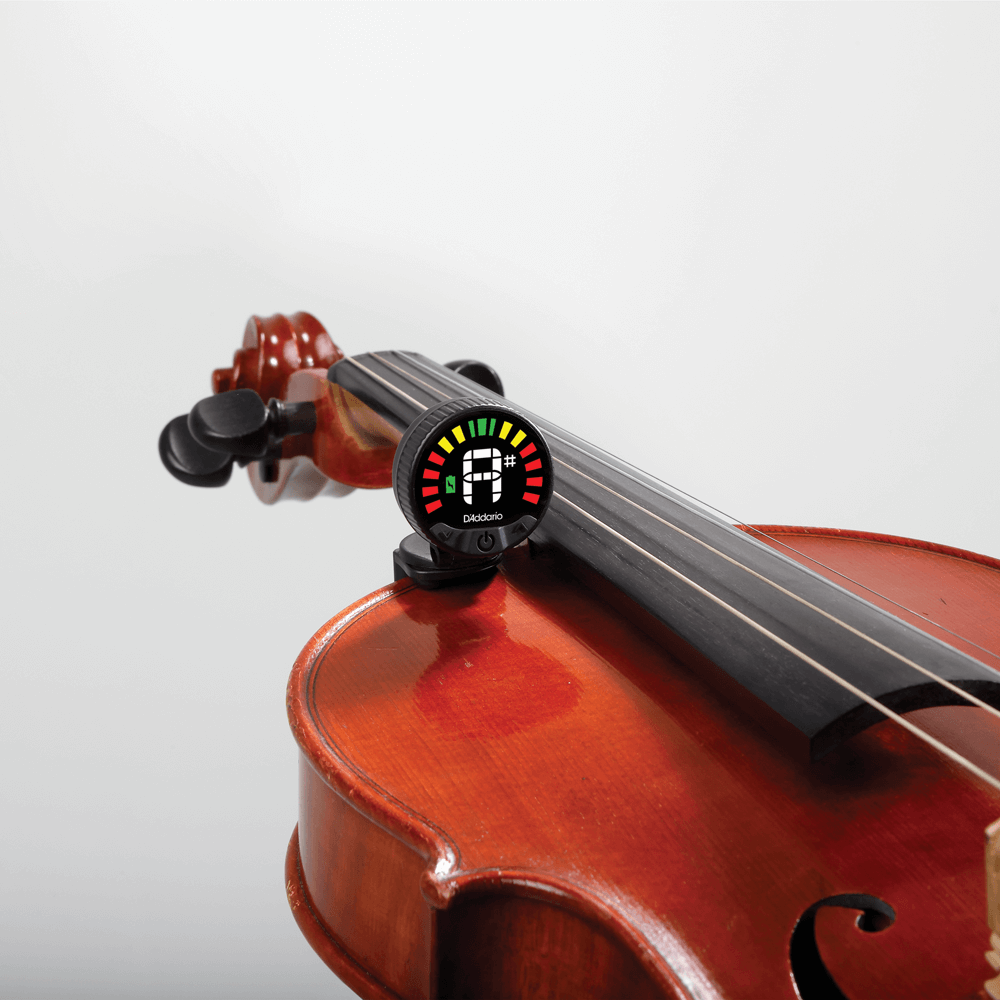The Nexxus 360 Violin Rechargeable Tuner is clipped to the neck of a violin, showing a tuning interface with colored bars and the letter A on its screen. The violin’s body and strings stand out against a white background, while the 360-degree LED display of the Nexxus 360 ensures easy viewing from any angle.