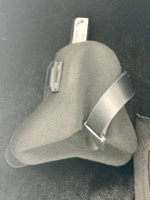 The Otto Musica Mirage CN-512 Oblong Violin Case features a black foam protective mask with an attached strap, resting on a dark surface, providing lightweight shielding reminiscent of the sleek protection within this premium violin case. Behind the mask, a metallic tag with text is partially visible.