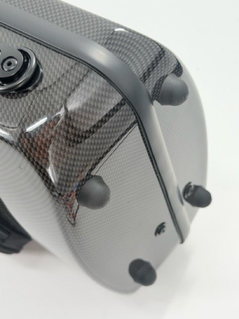Close-up of a gray carbon fiber Otto Musica Mirage CN-512 Oblong Violin Case, featuring four black rubber bumpers and a black circular component, set against a white background.
