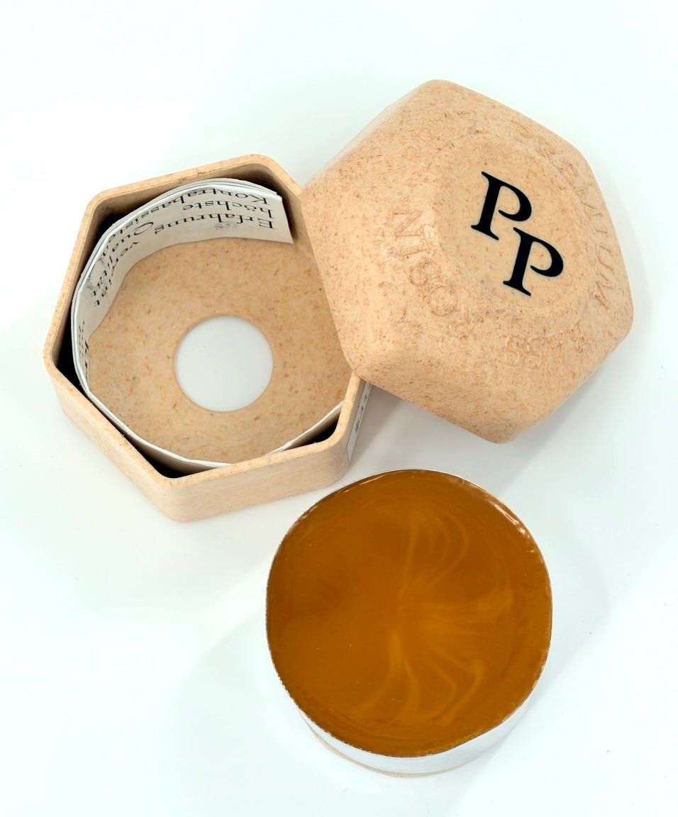 The Petz Premium Bass Rosin comes in a hexagonal beige container labeled "PP" on the lid, containing round, amber-colored premium rosin with an inner paper ring featuring text; shown open with both lid and rosin side by side.