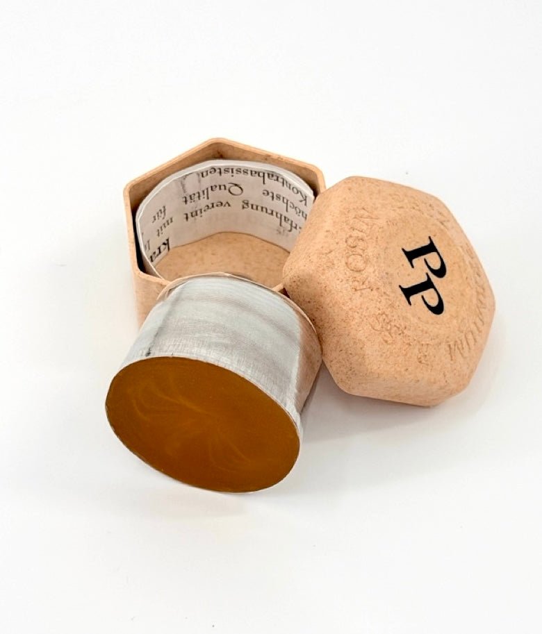 A hexagonal, cork-like container labeled "PP" on the lid is partly open to reveal a cylindrical bar of Petz Premium Bass Rosin inside, lined with printed paper.