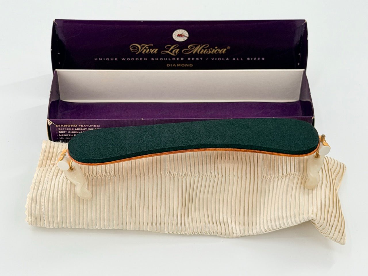 A Viva La Musica Diamond Shoulder Rest with a dark green pad, ivory feet, and wooden frame rests on a cream pouch in front of a purple Viva La Musica box.