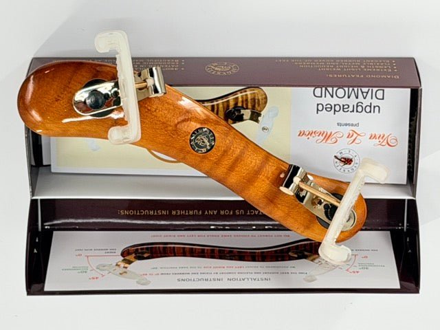 The Viva La Musica Diamond Violin Shoulder Rest – Light Varnish Maple Wood, featuring white plastic ends, is positioned atop an open product box that displays installation instructions and branding.